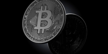Koyu zemin üzerinde duran, üzerinde Bitcoin simgesi bulunan metal para