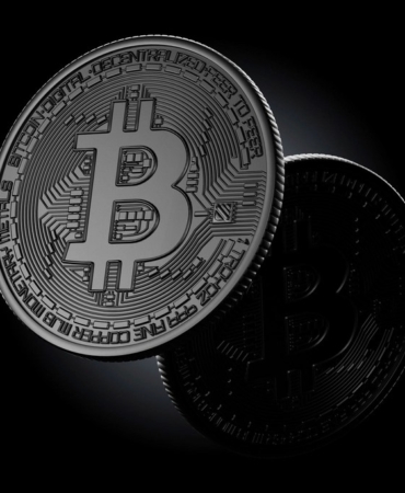 Koyu zemin üzerinde duran, üzerinde Bitcoin simgesi bulunan metal para