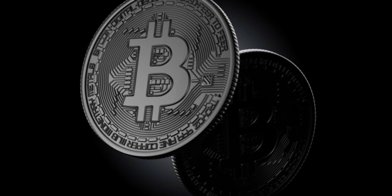 Koyu zemin üzerinde duran, üzerinde Bitcoin simgesi bulunan metal para