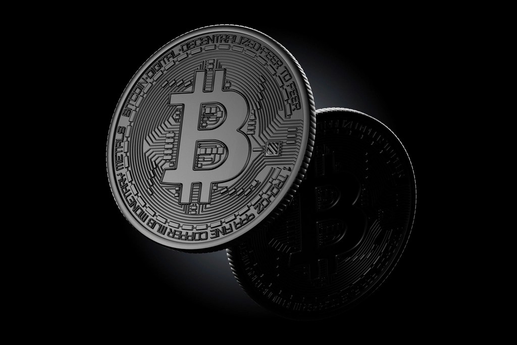 Koyu zemin üzerinde duran, üzerinde Bitcoin simgesi bulunan metal para