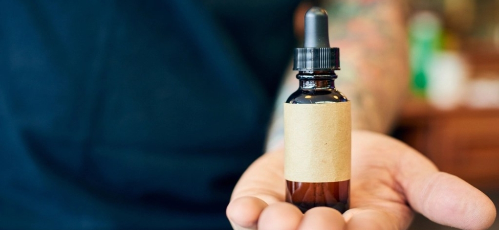 Damlalıklı küçük bir cam serum şişesini tutan bir el