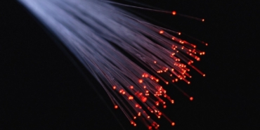 Karanlık zeminde uçları kırmızı ışıkla parlayan fiber optik lif demeti