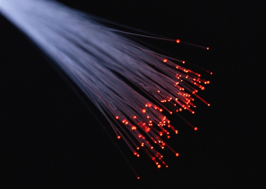 Karanlık zeminde uçları kırmızı ışıkla parlayan fiber optik lif demeti