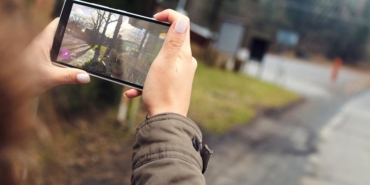 İki eliyle tuttuğu akıllı telefonla açık havada fotoğraf çeken bir kişinin elleri