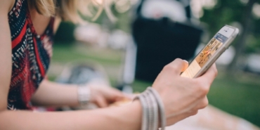 Oturan bir kişinin iki eliyle tuttuğu akıllı telefon yakından görülüyor