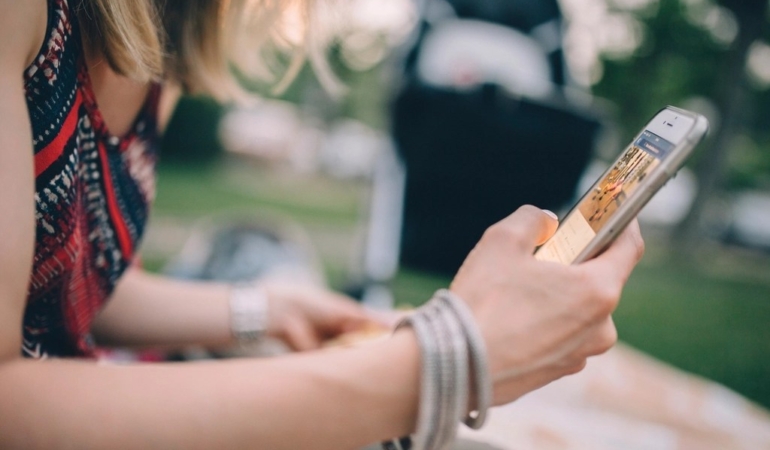 Oturan bir kişinin iki eliyle tuttuğu akıllı telefon yakından görülüyor