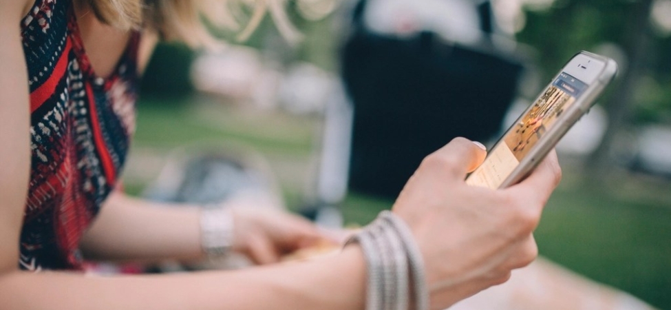 Oturan bir kişinin iki eliyle tuttuğu akıllı telefon yakından görülüyor