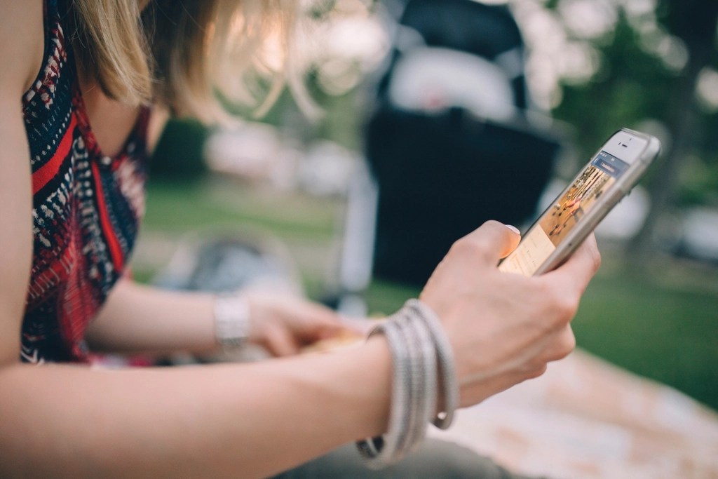 Oturan bir kişinin iki eliyle tuttuğu akıllı telefon yakından görülüyor