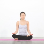 Mat üzerinde bağdaş kurarak meditasyon yapan kadın