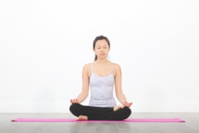 Mat üzerinde bağdaş kurarak meditasyon yapan kadın