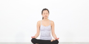 Mat üzerinde bağdaş kurarak meditasyon yapan kadın