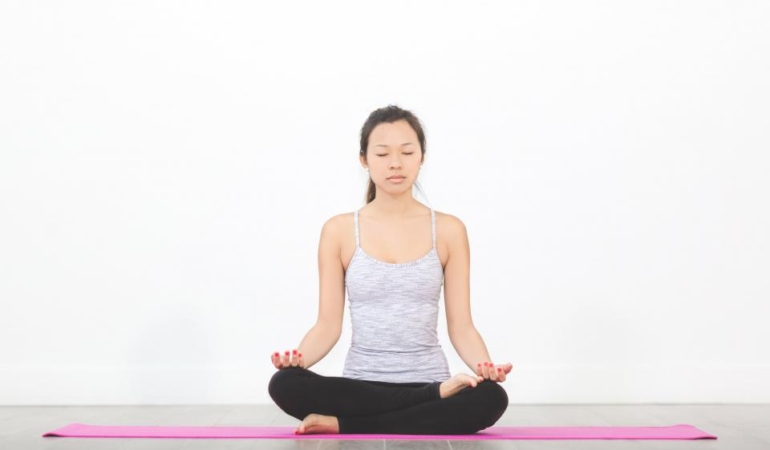 Mat üzerinde bağdaş kurarak meditasyon yapan kadın