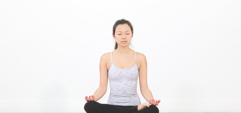 Mat üzerinde bağdaş kurarak meditasyon yapan kadın
