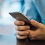 İki eliyle akıllı telefon tutan ve ekrana dokunan bir kişinin elleri