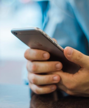 İki eliyle akıllı telefon tutan ve ekrana dokunan bir kişinin elleri