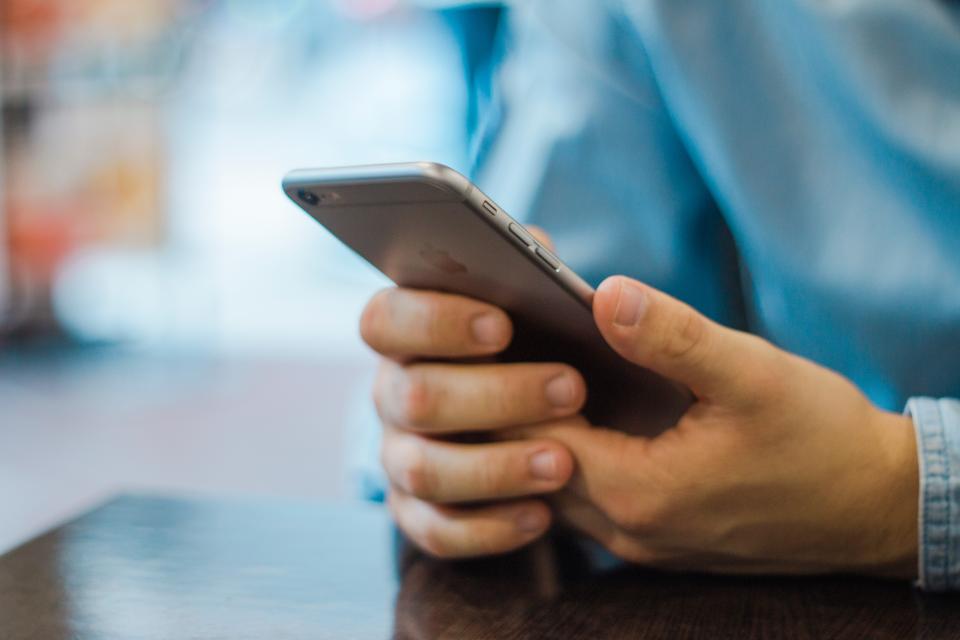 İki eliyle akıllı telefon tutan ve ekrana dokunan bir kişinin elleri