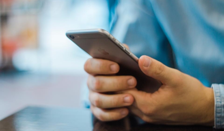 İki eliyle akıllı telefon tutan ve ekrana dokunan bir kişinin elleri