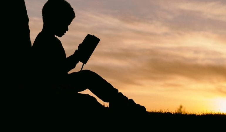 Gün batımında dışarıda oturmuş kitap okuyan bir kişinin silueti