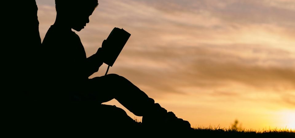 Gün batımında dışarıda oturmuş kitap okuyan bir kişinin silueti