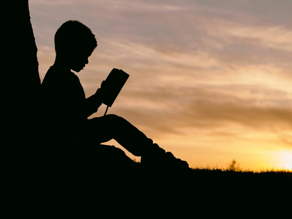 Gün batımında dışarıda oturmuş kitap okuyan bir kişinin silueti