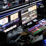 Karanlık bir odada birden fazla monitörün açık olduğu bilgisayar masası