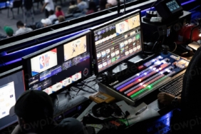 Karanlık bir odada birden fazla monitörün açık olduğu bilgisayar masası