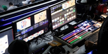 Karanlık bir odada birden fazla monitörün açık olduğu bilgisayar masası
