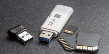 Koyu zemin üzerinde duran beyaz bir USB bellek ve küçük bir kart okuyucu