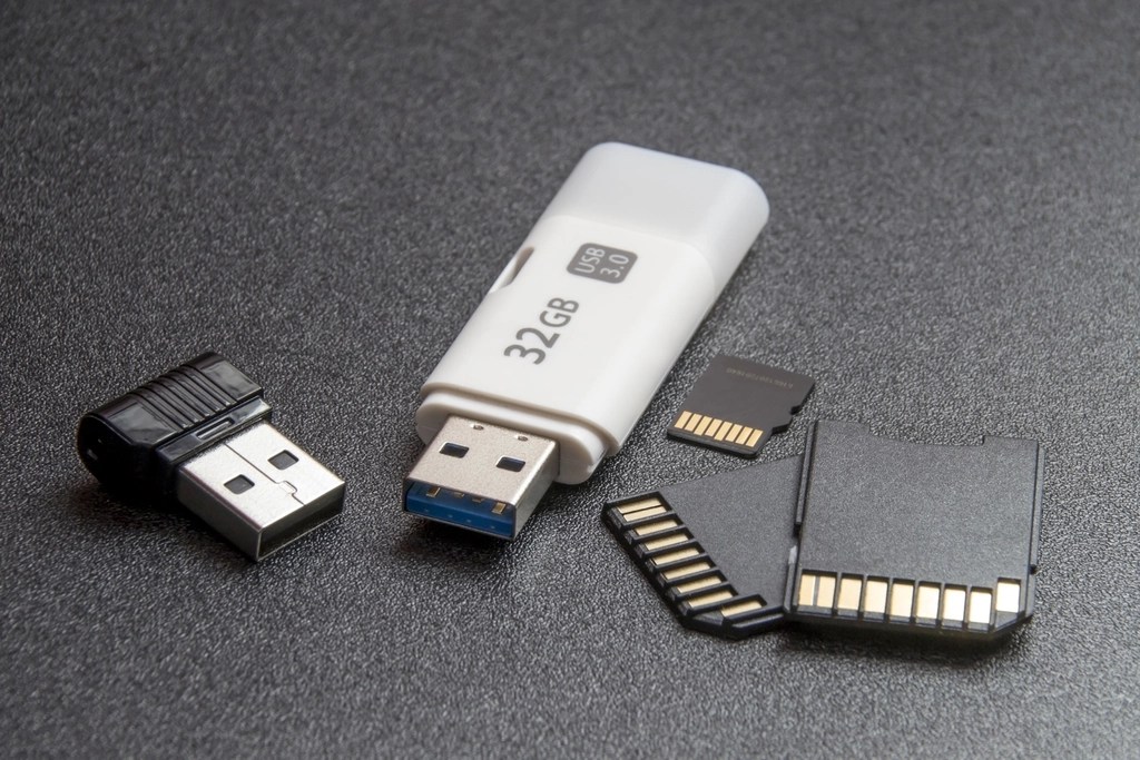 Koyu zemin üzerinde duran beyaz bir USB bellek ve küçük bir kart okuyucu